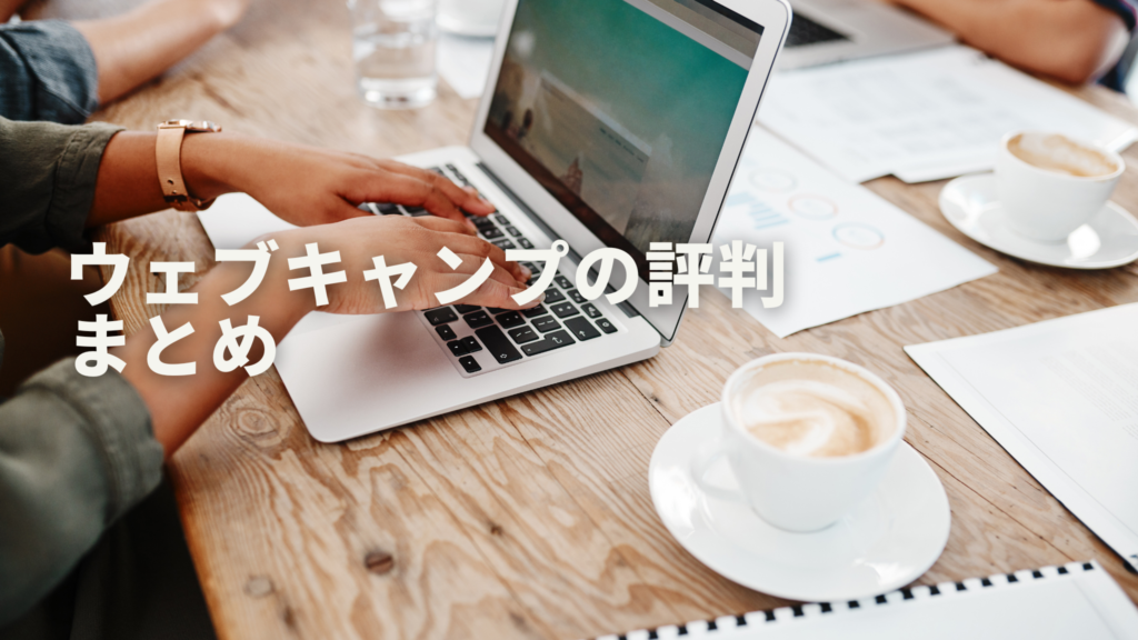 木目調のテーブルの上でパソコン作業する女性の手元と、横にカフェラテが置いてあって、チームメイトと一緒に作業している