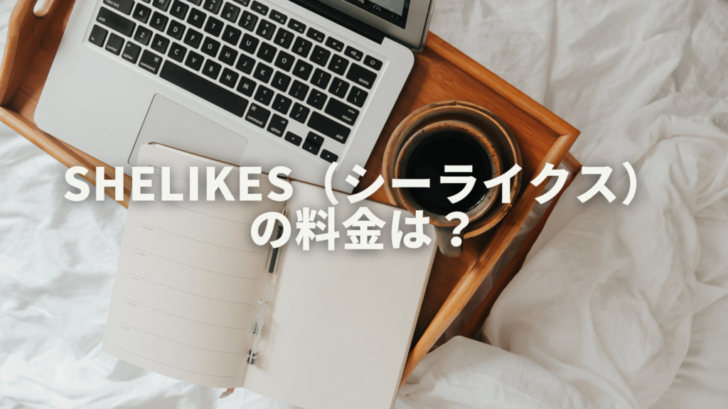 白い布団の上に木のトレーがあり、その上にノート、パソコン、コーヒーが置かれています